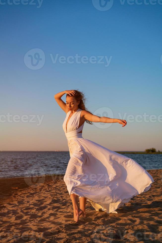 lindo menina dentro uma grandes branco vestir de a mar dentro a tarde às pôr do sol foto