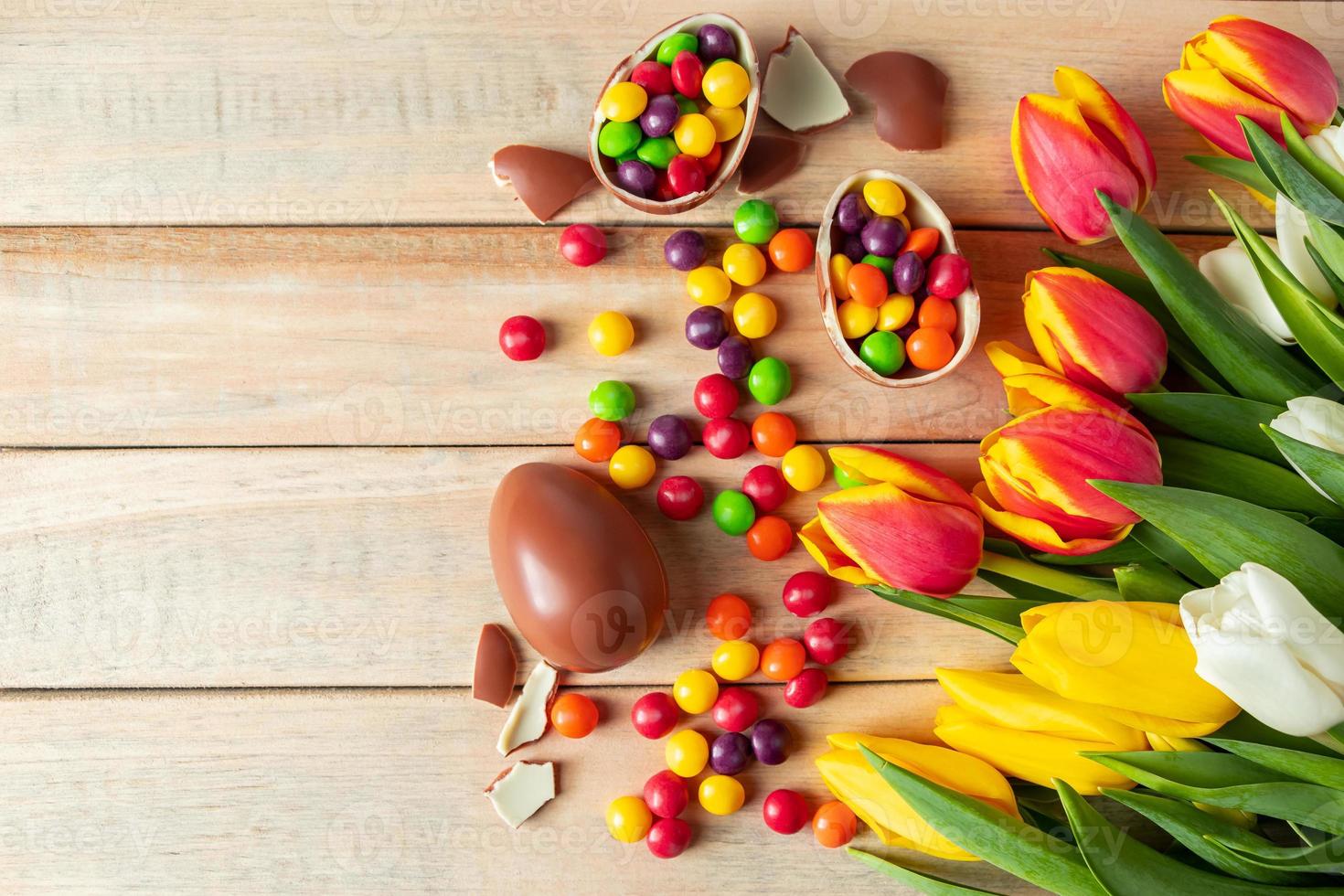 lindas tulipas vermelhas e amarelas para o feriado da Páscoa. ovos de chocolate e doces em um fundo de madeira. foto