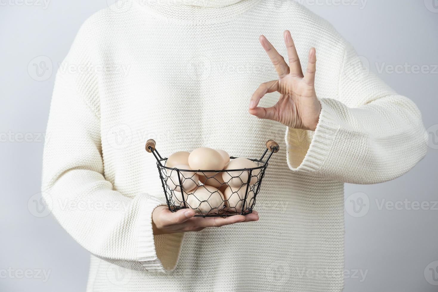 mãos femininas com uma cesta metálica de ovos de galinha crus fazendo um gesto de ok foto