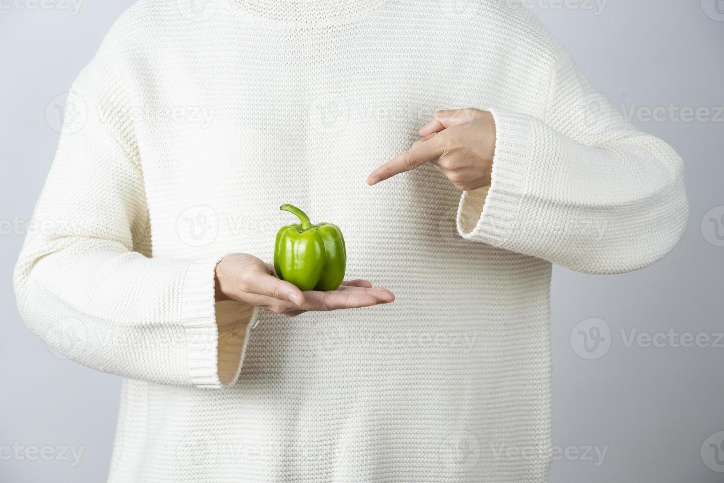 mãos femininas segurando e apontando para um pimentão verde foto