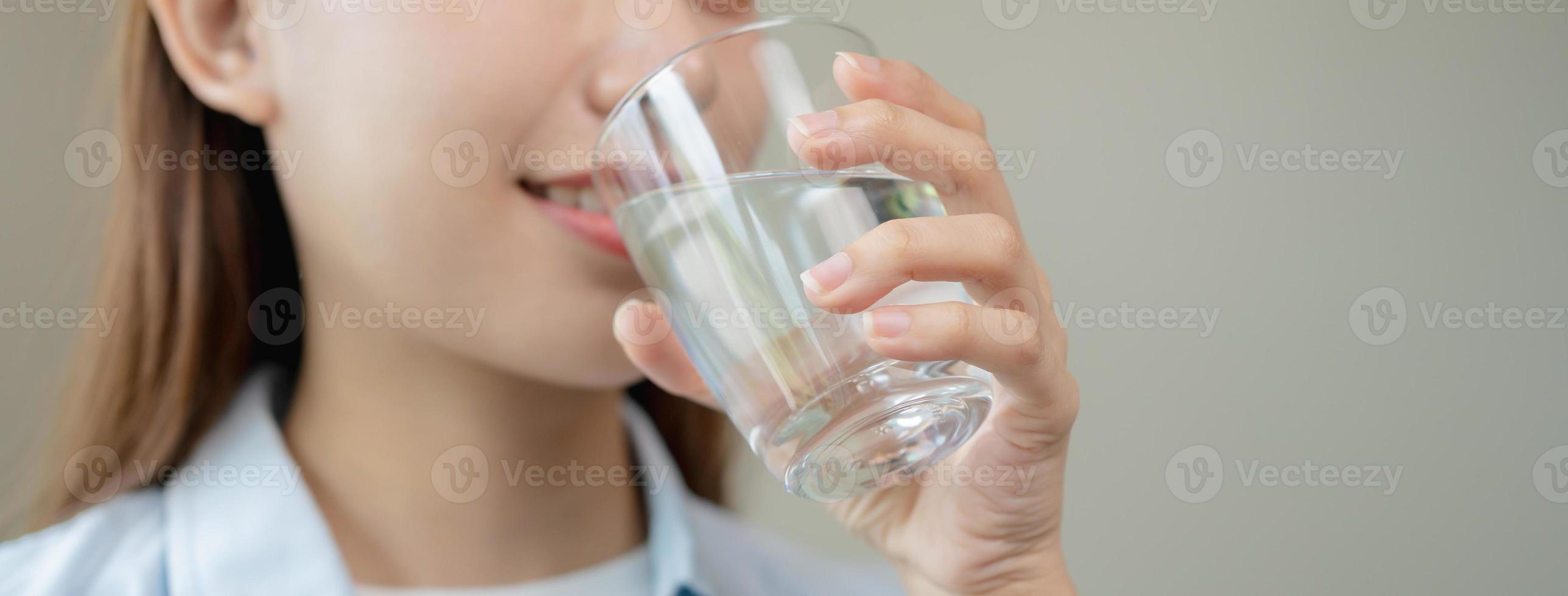 feliz lindo, mão do ásia jovem mulher bebendo, trago fresco vidro do água para hidratação do corpo, segurando transparente vidro dentro dela mão, com sede às lar. saúde Cuidado, saudável estilo de vida conceito. foto