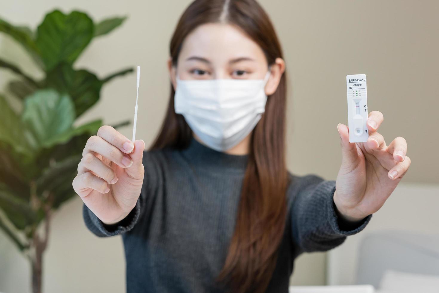 pandemia do doença, sorrir ásia jovem mulher, menina mão mostrar segurando atk, antígeno kit auto teste. apresentando dispositivo nasal, nariz cotonete teste para possível infecção do coroa, cobiçado às lar. saúde Cuidado. foto