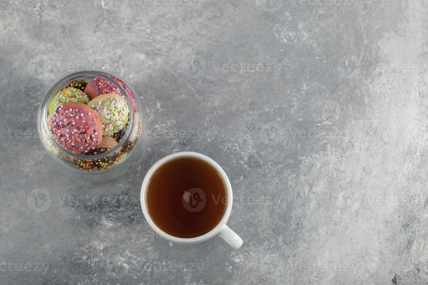 uma jarra de vidro cheia de pequenos donuts coloridos com uma xícara de chá quente foto