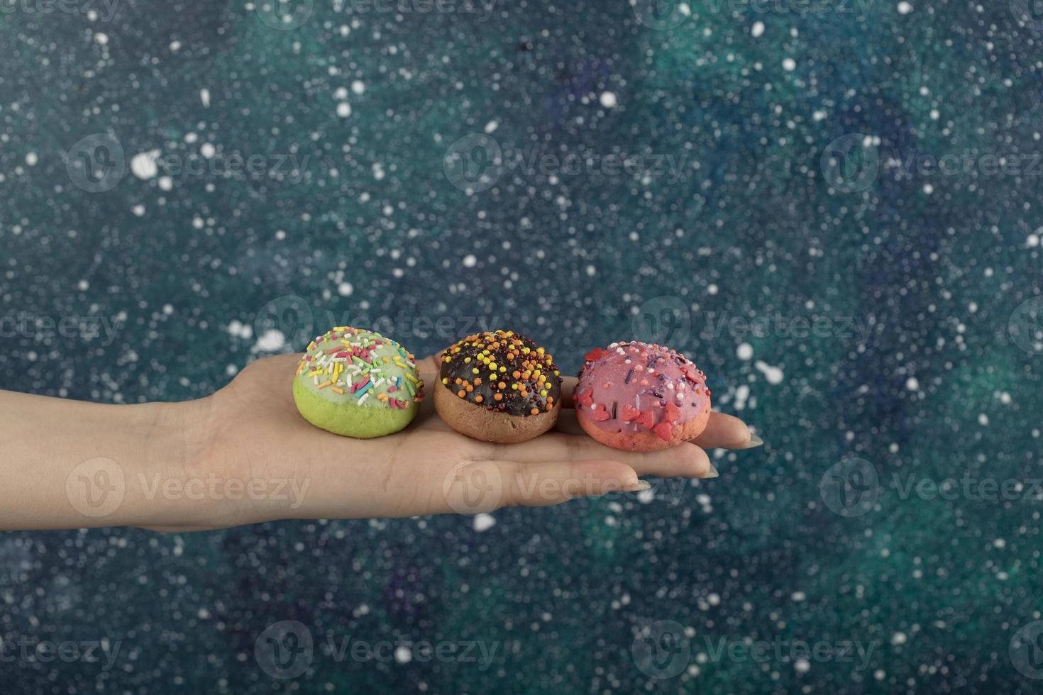 mão de uma mulher segurando rosquinhas doces coloridas com granulado foto