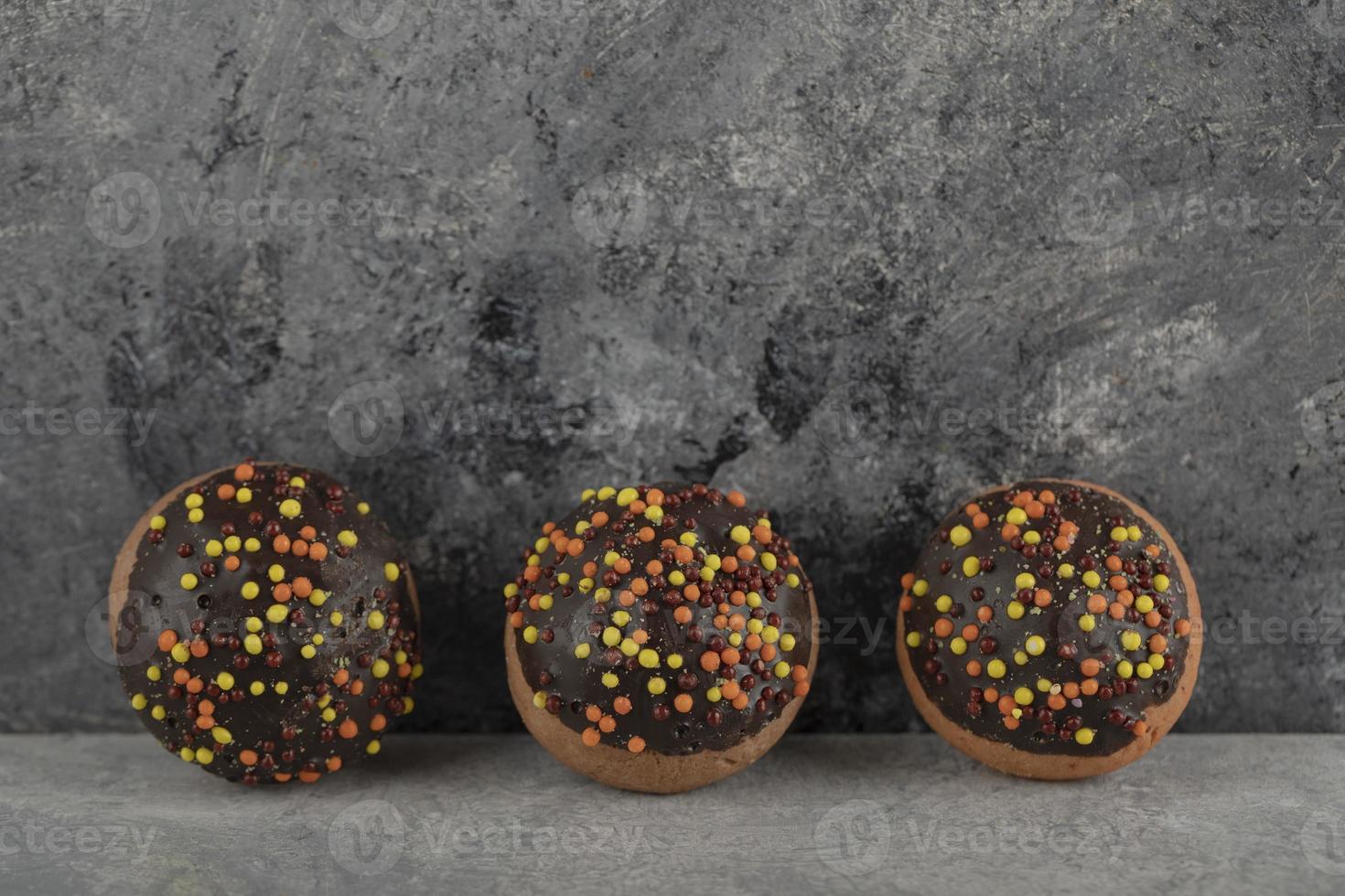 três donuts doces de chocolate com granulado foto