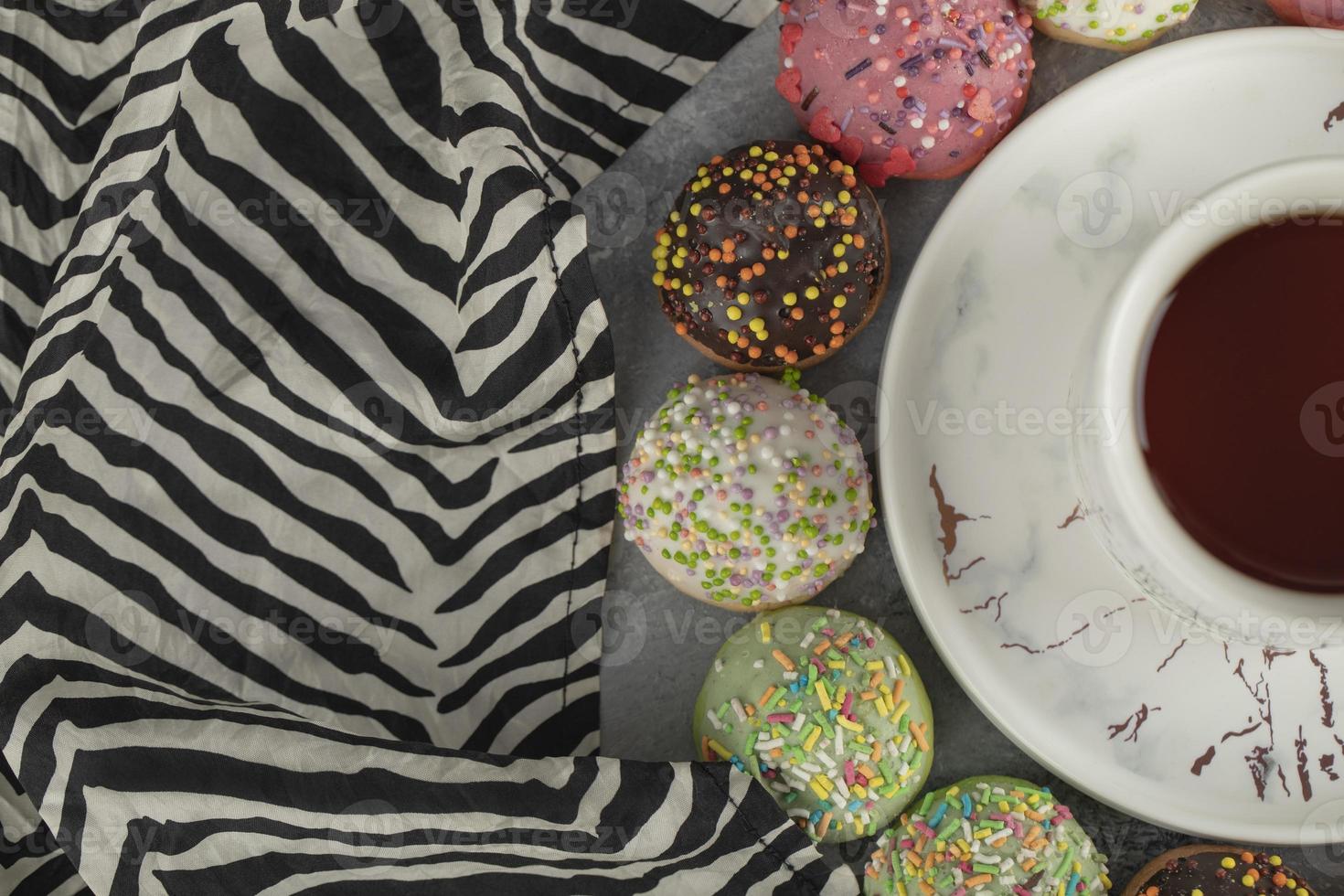 rosquinhas doces e coloridas com granulado e uma xícara de chá foto