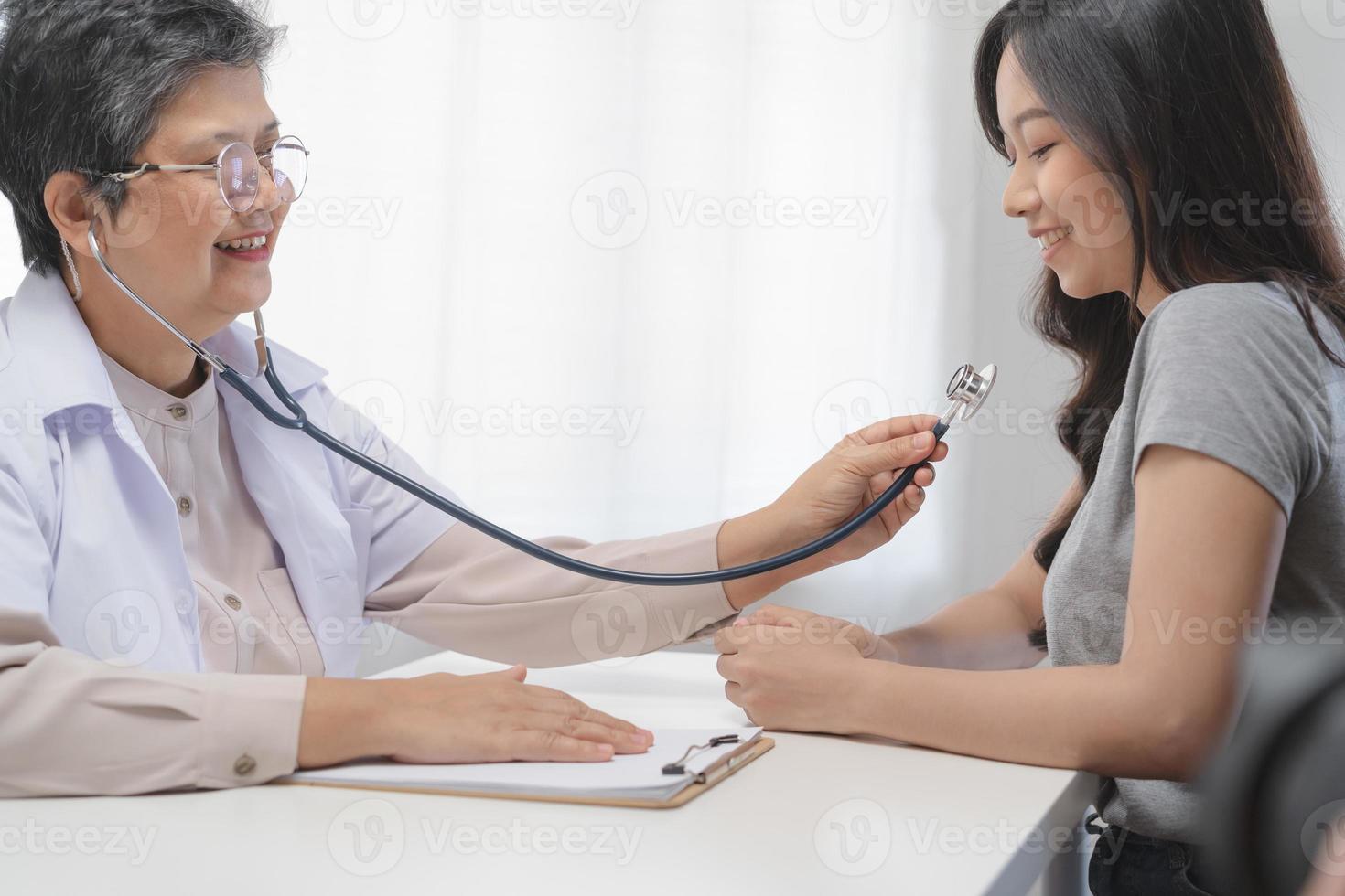 maduro, Senior ásia médico, psiquiatra, geral mulher médico consultando preocupado com jovem paciente, usando estetoscópio para ouvir, compromisso às clínica, hospital. saúde Cuidado, Verifica acima médico. foto