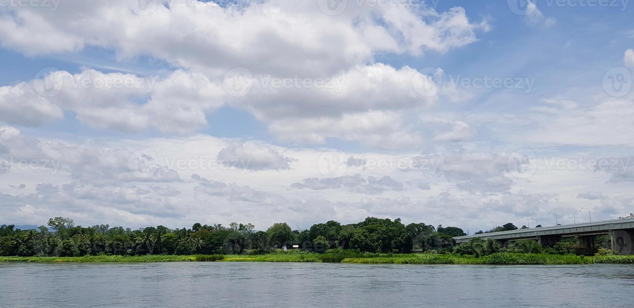 lindo azul céu com rodovia ou ponte através rio de veículo, branco nuvens e verde árvore para fundo. transporte, estrutura, beleza do natureza e natural papel de parede concep foto