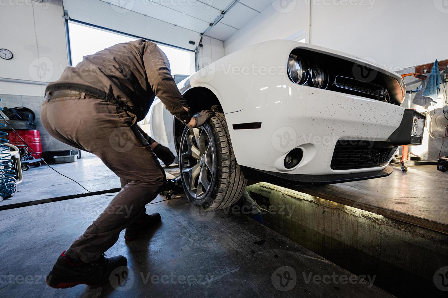 mecânico na estação de reparação de serviço trabalhando com muscle car. inspeciona a parte móvel da roda. foto