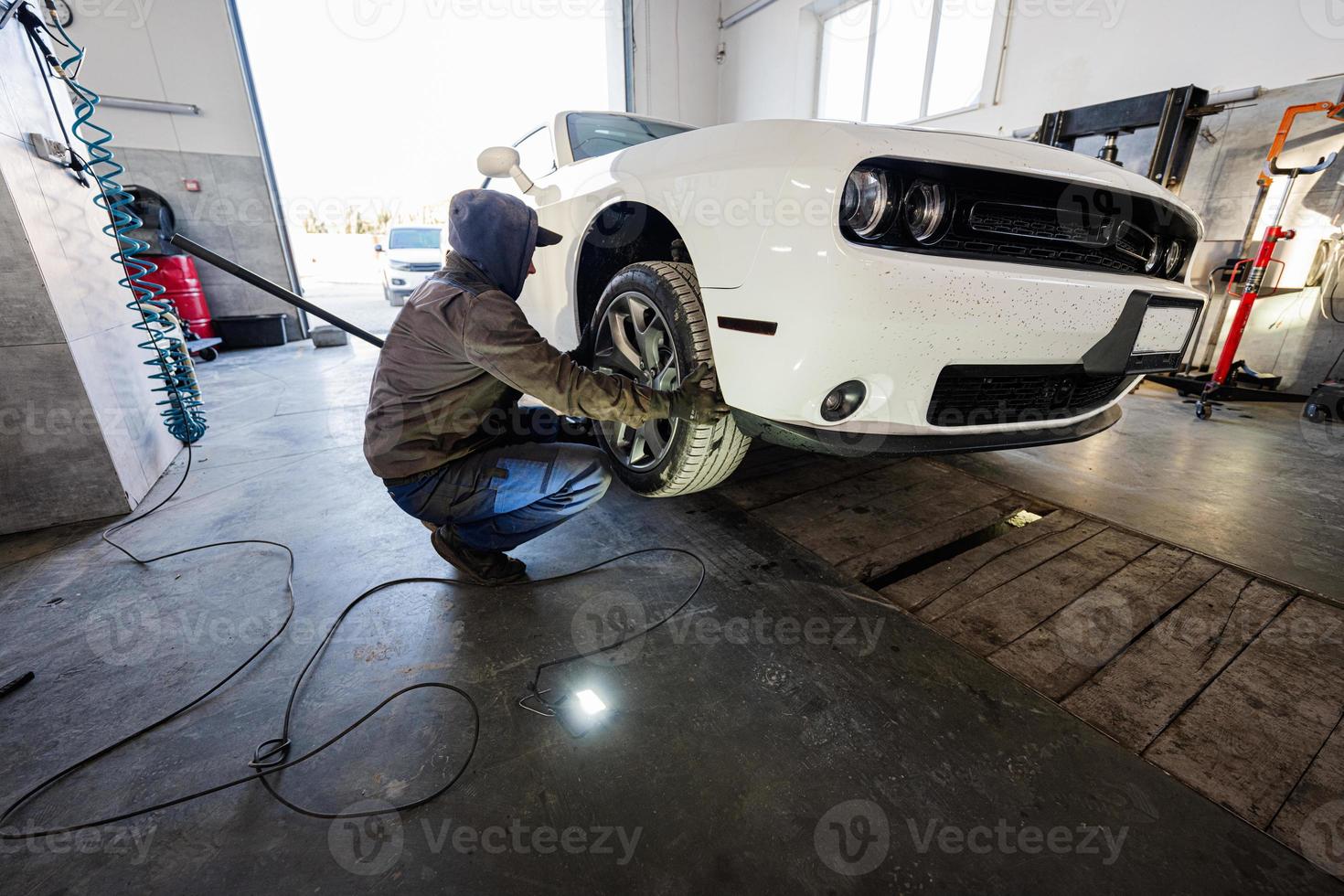 mecânico na estação de reparação de serviço trabalhando com muscle car. homem trabalhador levanta o carro para diagnosticar o chassi. foto