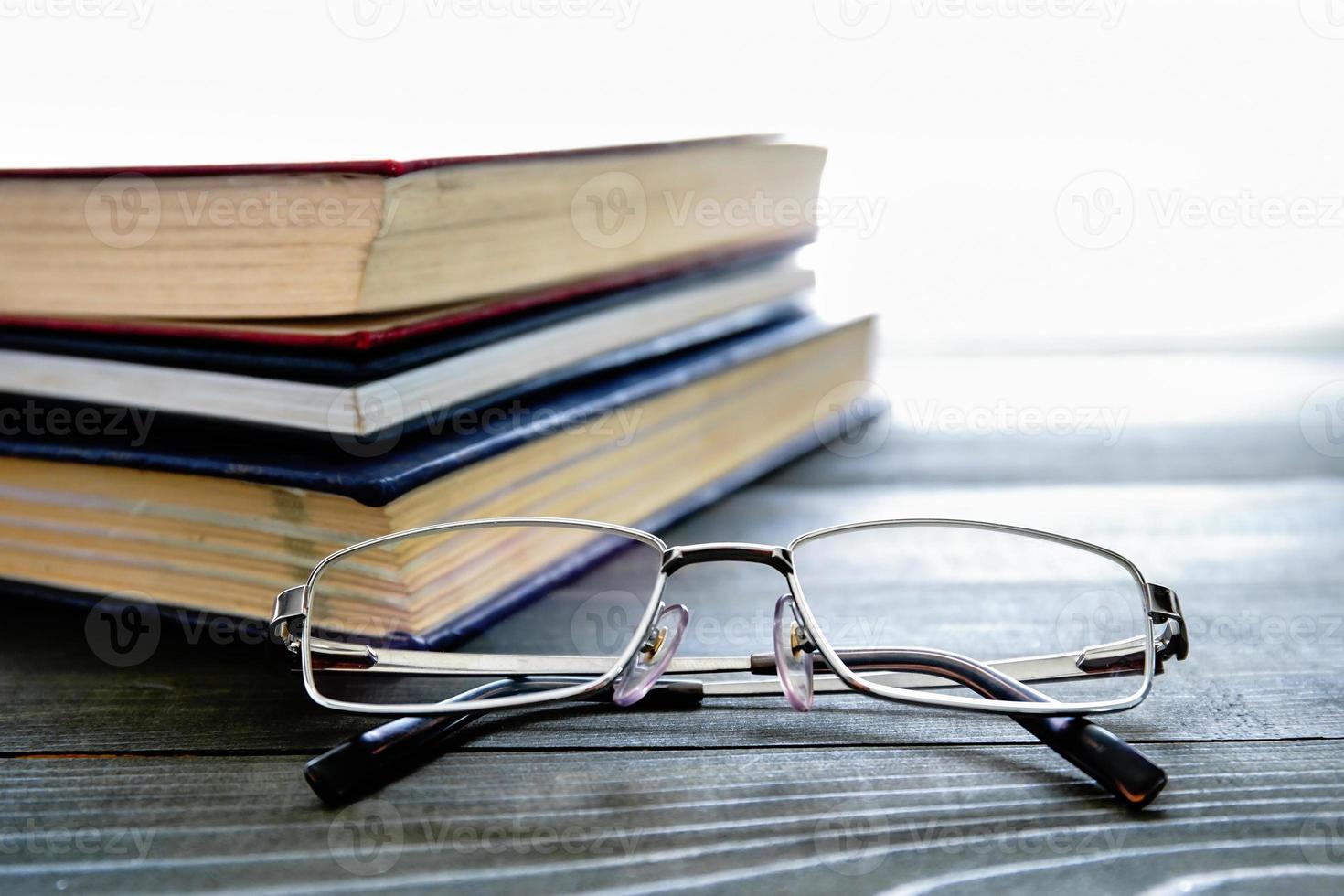 óculos e pilha de livros de capa dura foto