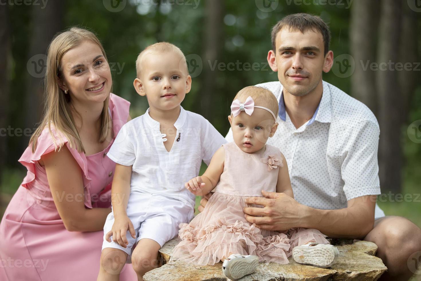 marido e esposa e seus pequeno crianças. família retrato dentro natureza. mãe e Papai estão posando com seus irmão e irmã. jovem família com crianças para uma andar dentro a madeiras. foto