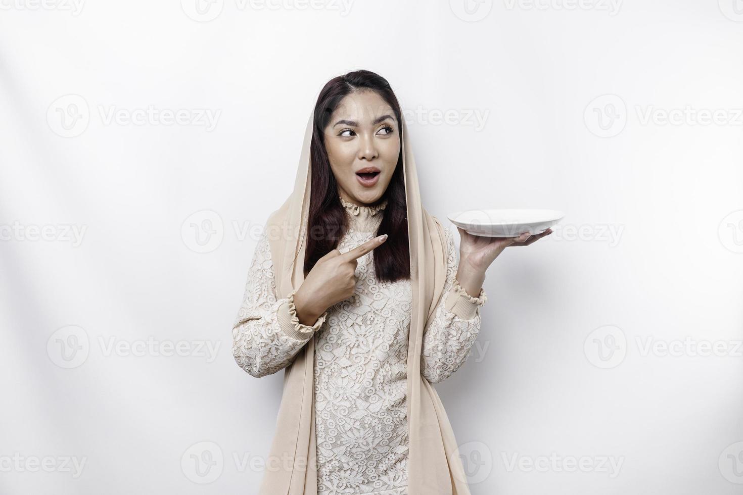 a ásia muçulmano mulher é jejum e com fome e segurando utensílios talheres enquanto olhando a parte, de lado pensando sobre o que para comer foto