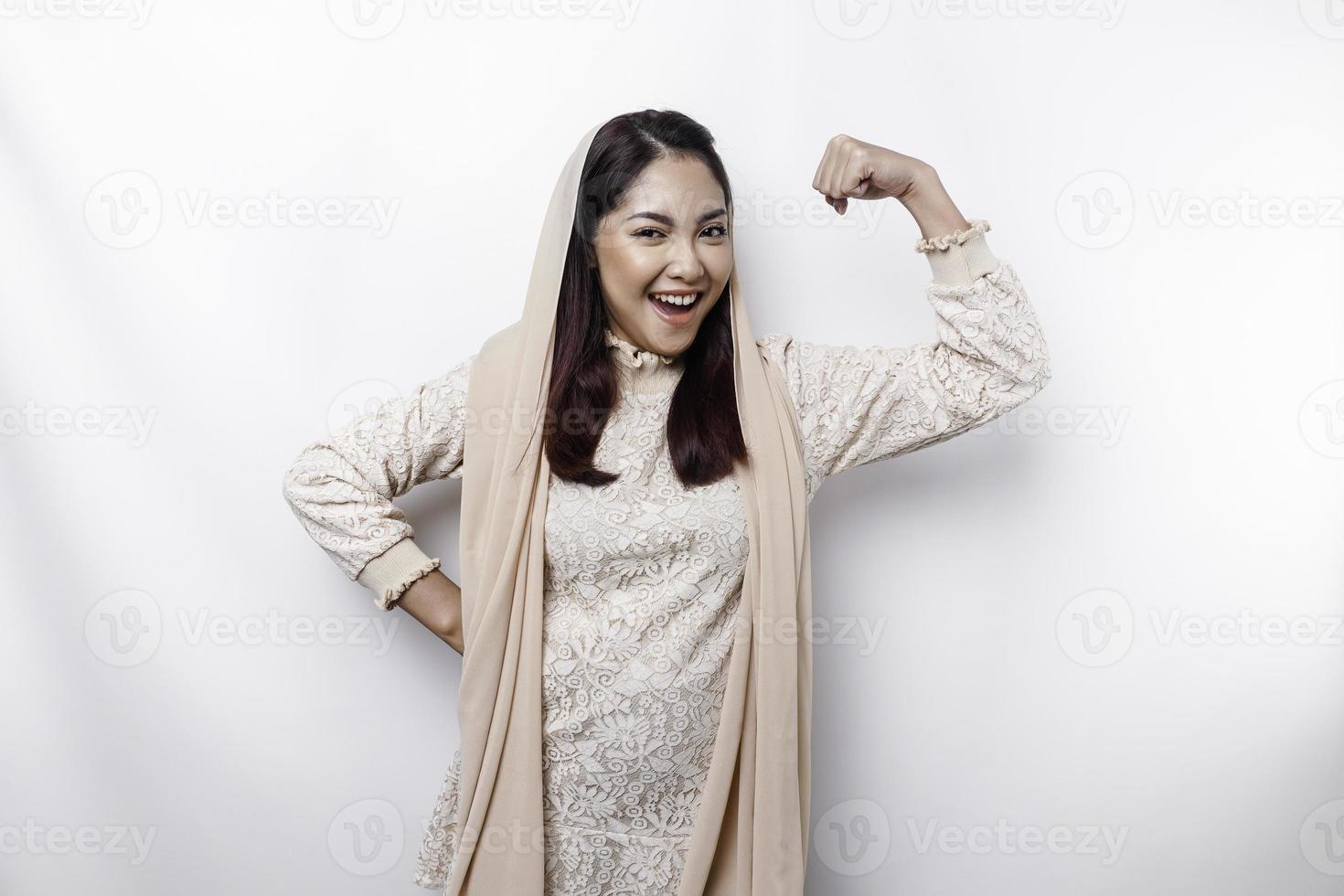 animado ásia muçulmano mulher vestindo uma lenço de cabeça mostrando Forte gesto de elevação dela braços e músculos sorridente orgulhosamente foto