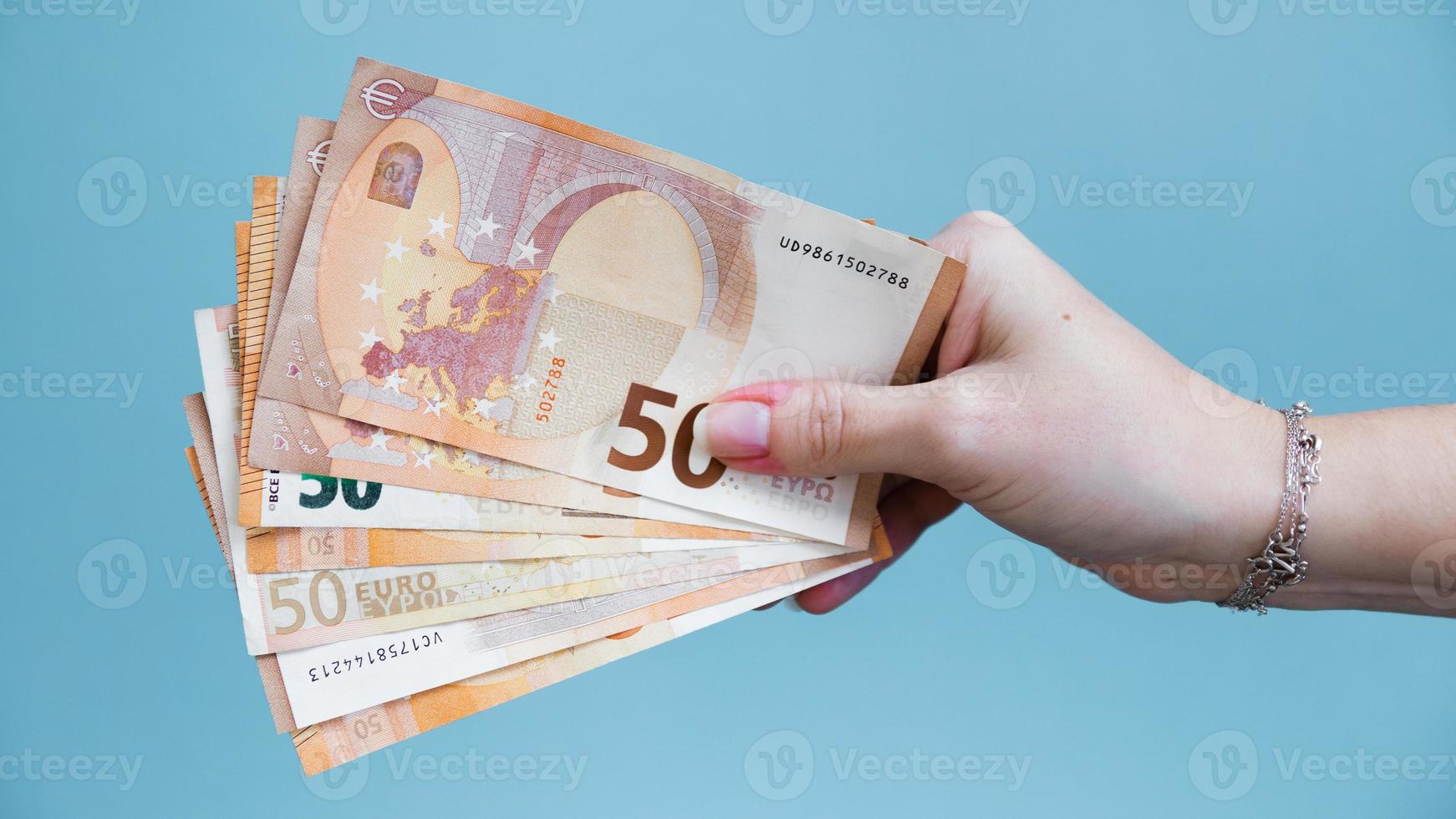 mulher mão segurando cinquenta euro notas em uma azul fundo. foto
