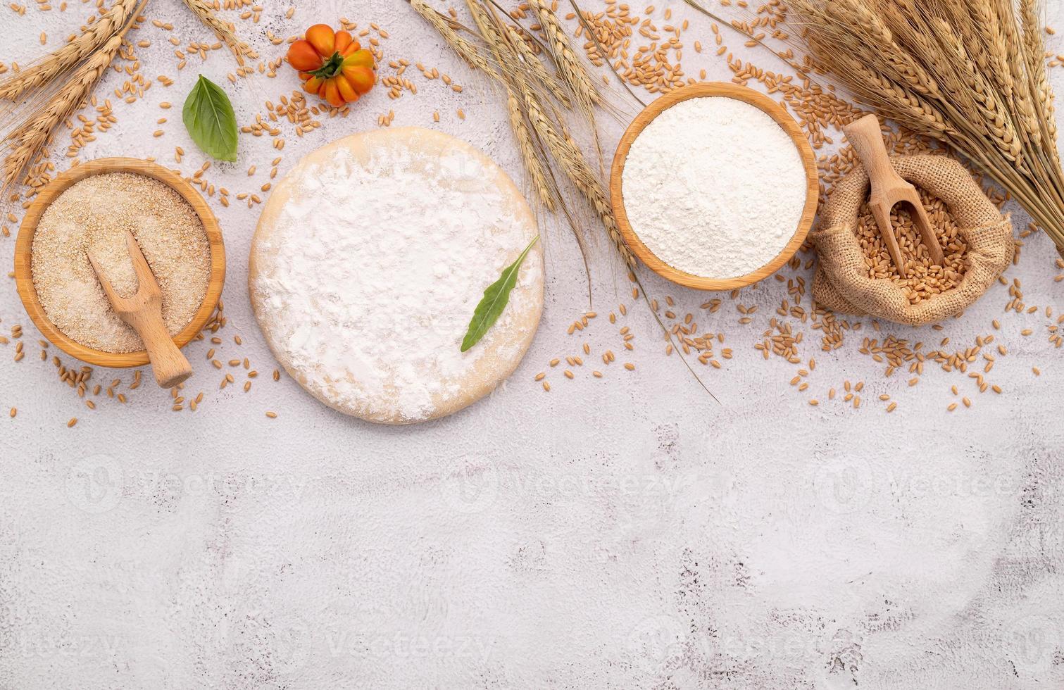 os ingredientes para massa de pizza caseira com espigas de trigo, farinha de trigo e grãos de trigo configurados em fundo branco de concreto. foto