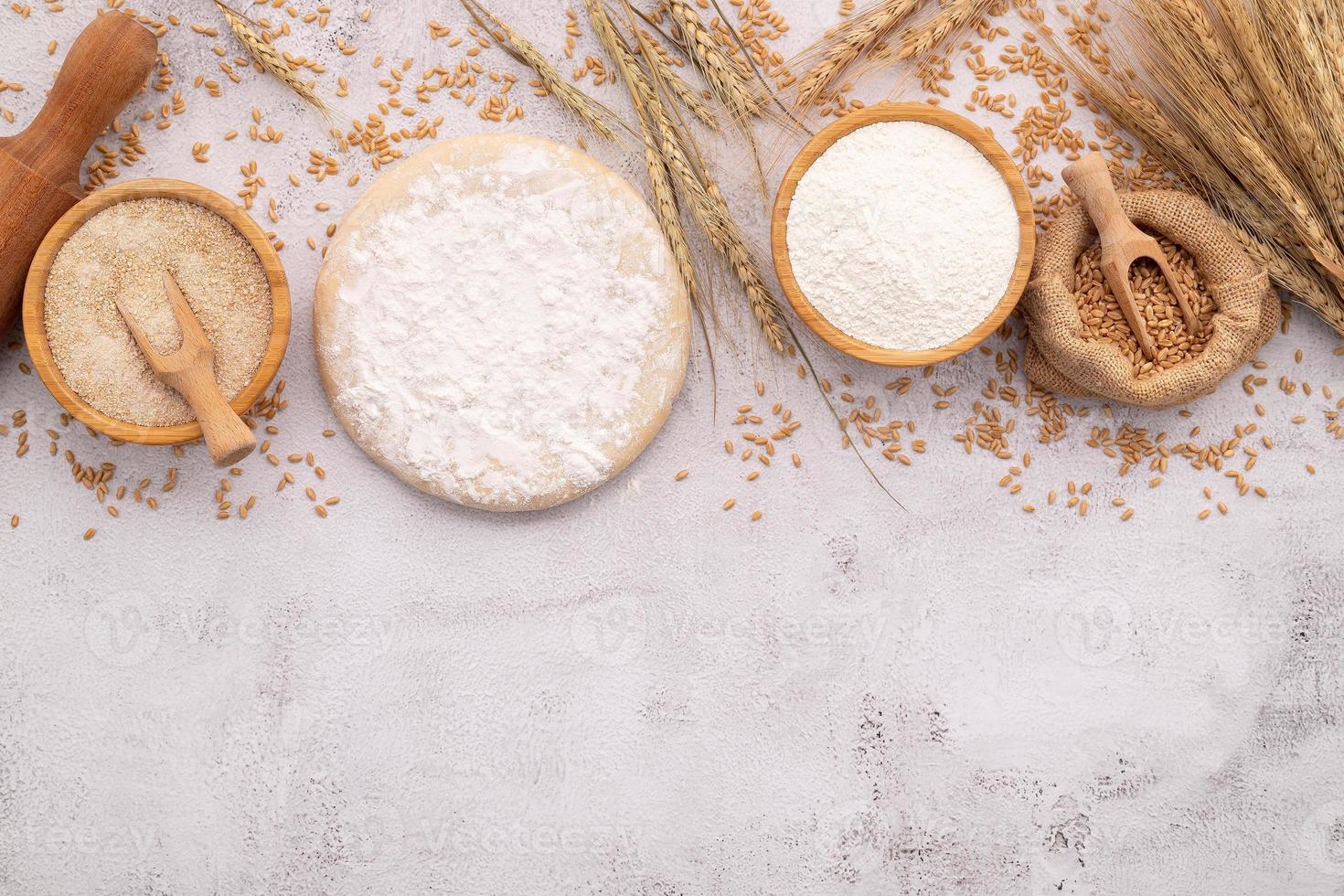 os ingredientes para massa de pizza caseira com espigas de trigo, farinha de trigo e grãos de trigo configurados em fundo branco de concreto. foto
