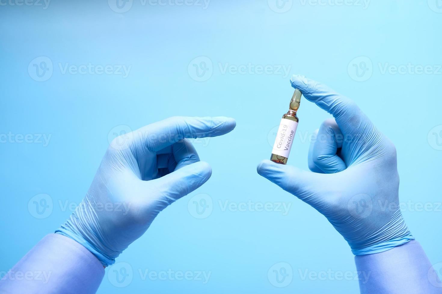 mão em luvas de látex segurando vacina covid-19 em fundo azul foto