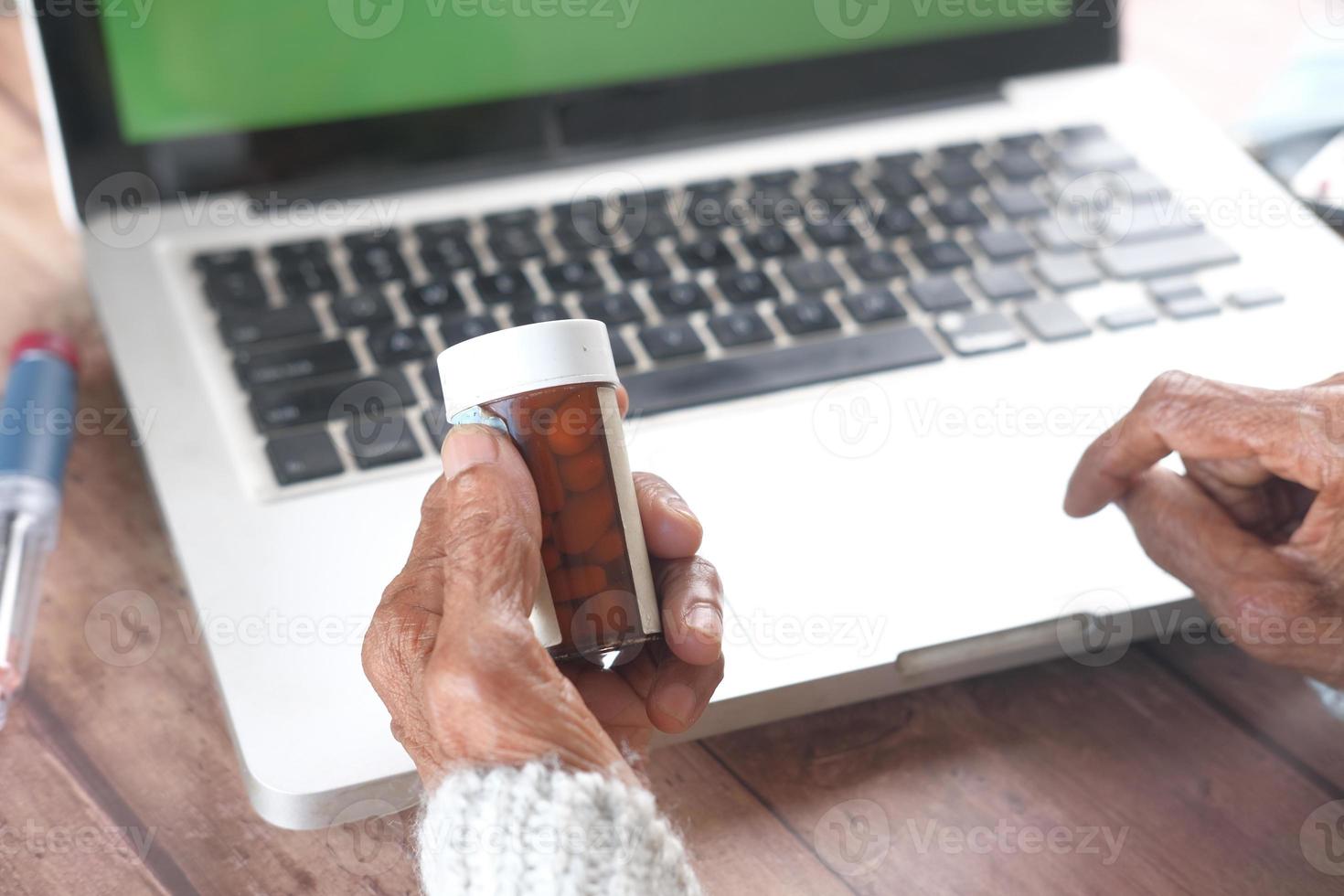 mão de uma mulher segurando o frasco de comprimidos enquanto está sentada em um computador foto