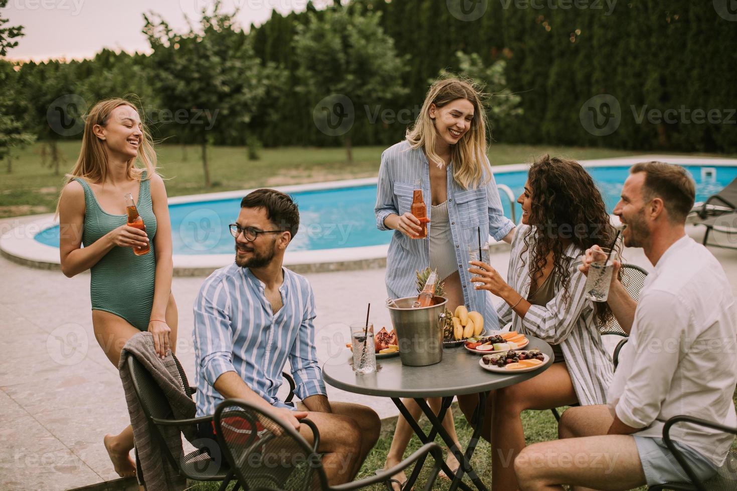 grupo de jovens torcendo com cidra à beira da piscina no jardim foto