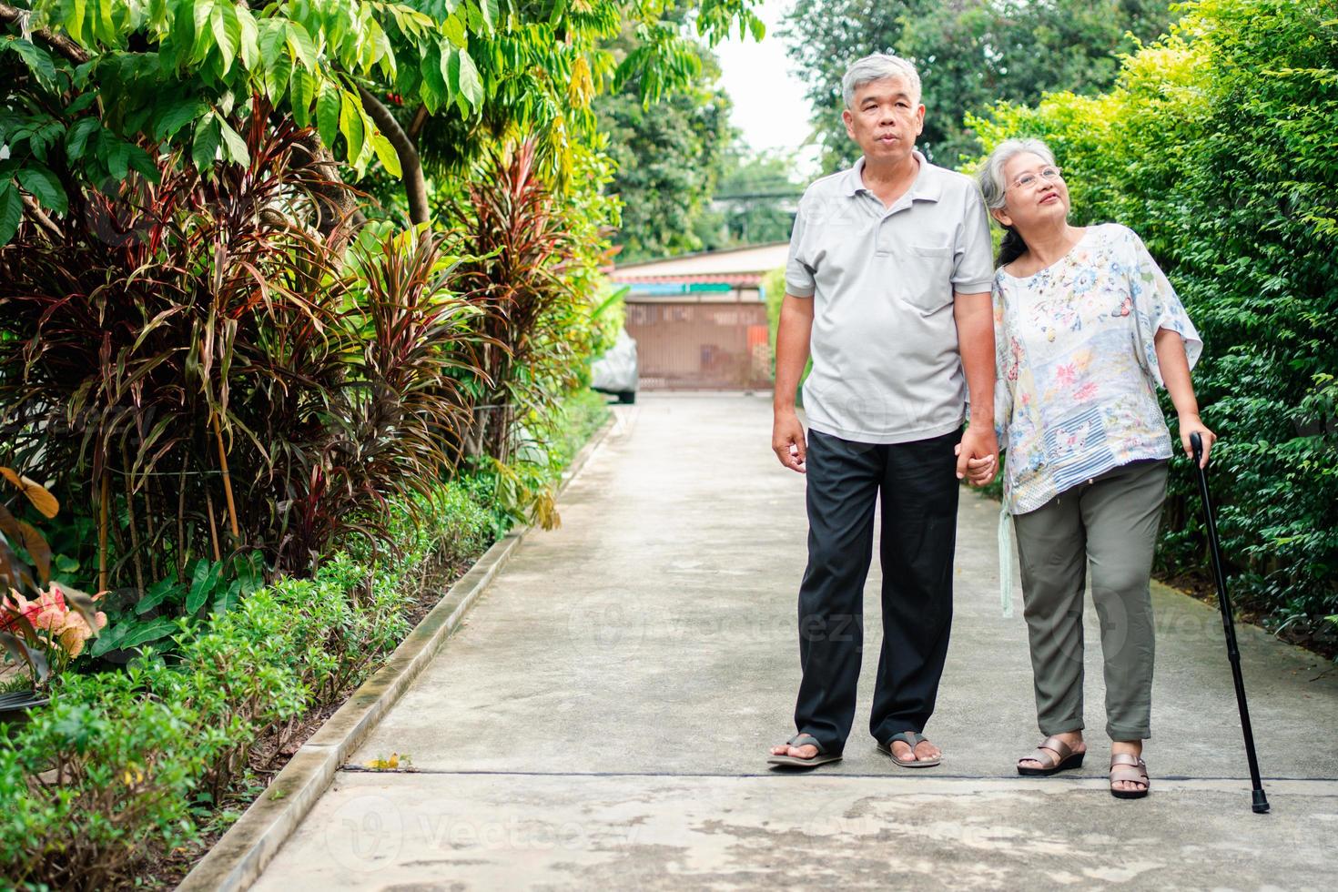 feliz Senior casal caminhando juntos dentro a jardim. velho idosos usando uma caminhando bastão para Socorro andar equilíbrio. conceito do amor e Cuidado do a família e saúde seguro para família foto