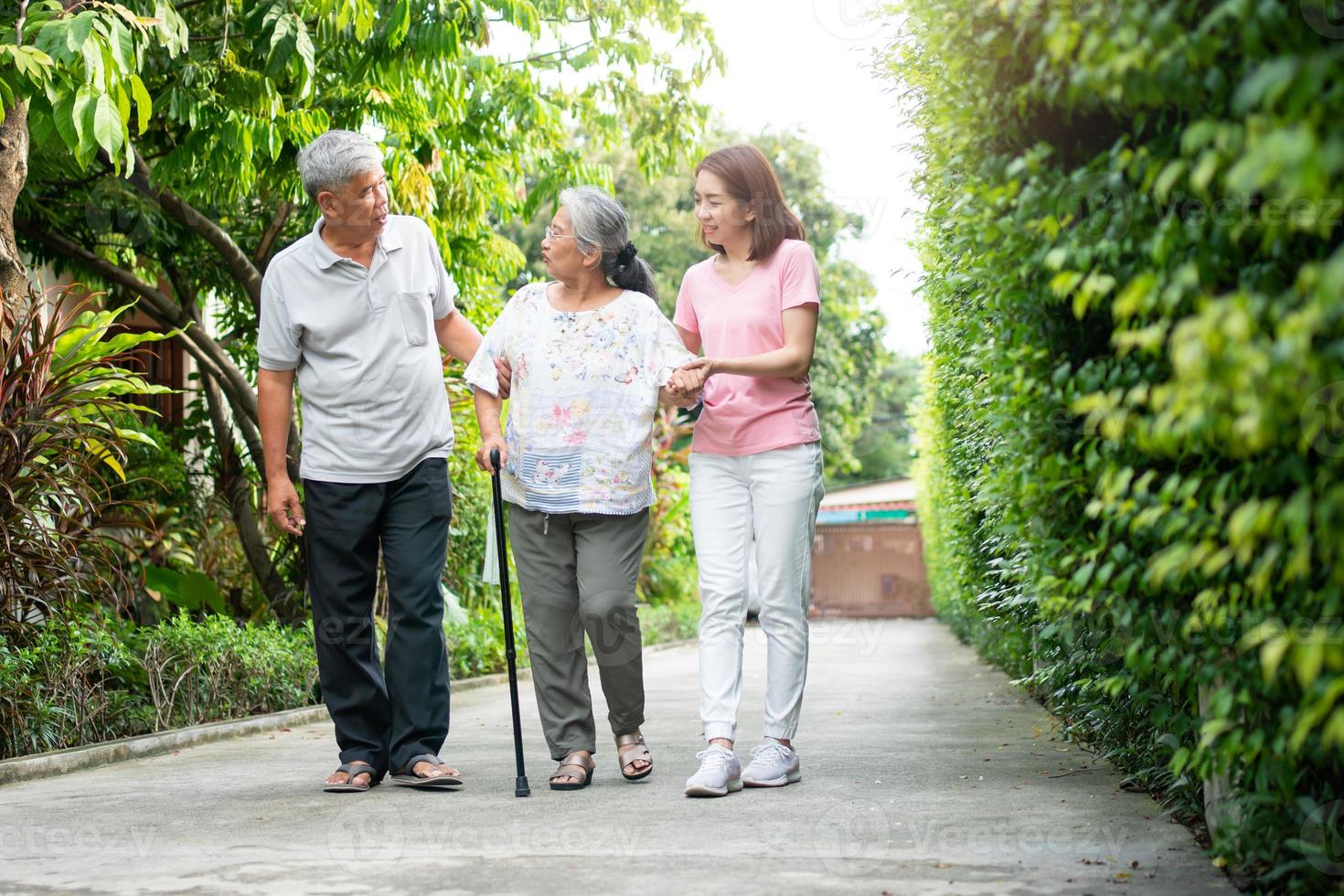 feliz família caminhando juntos dentro a jardim. velho idosos usando uma caminhando bastão para Socorro andar equilíbrio. conceito do amor e Cuidado do a família e saúde seguro para família foto