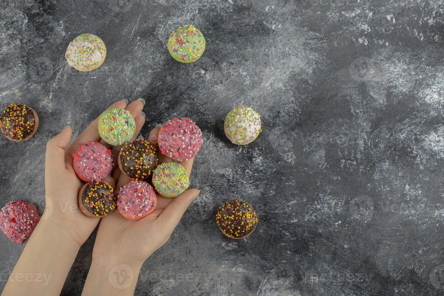 mãos segurando rosquinhas pequenas e coloridas com granulado foto