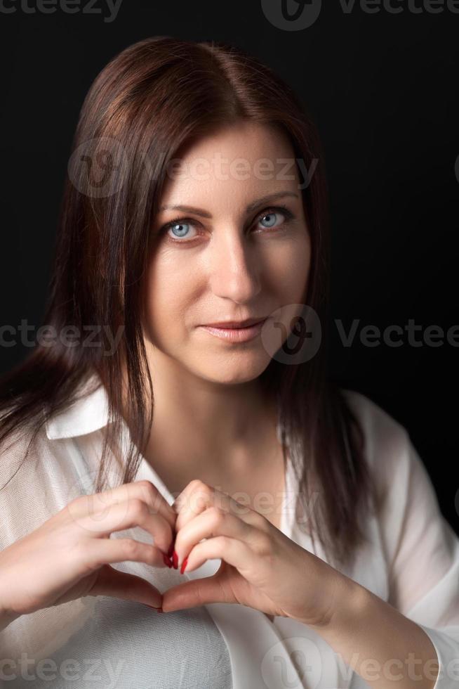 retrato do mulher mostrando coração formas placa com ambos mãos e olhando às Câmera foto