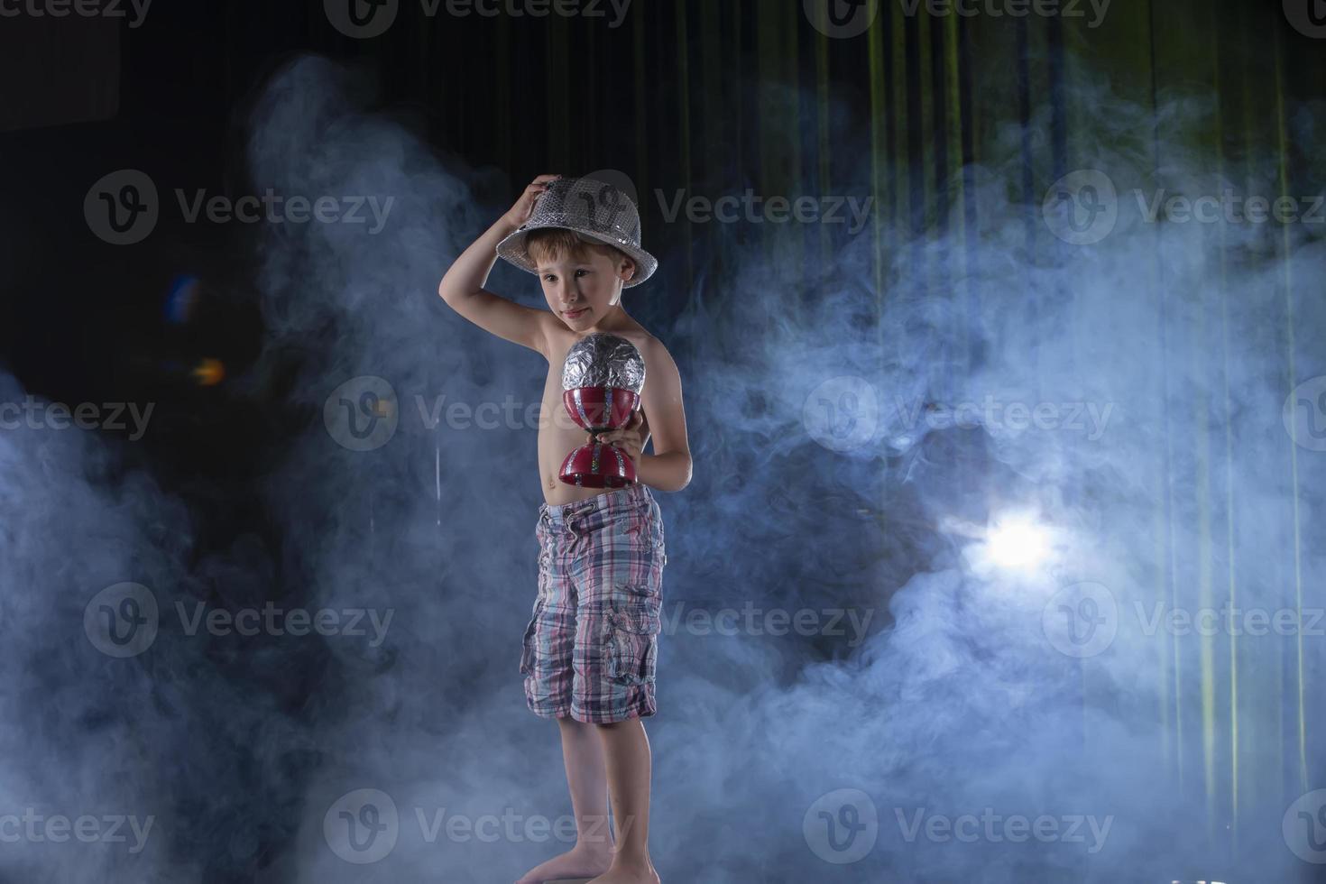 uma pequeno Garoto circo artista executa contra a pano de fundo do etapa iluminação. foto