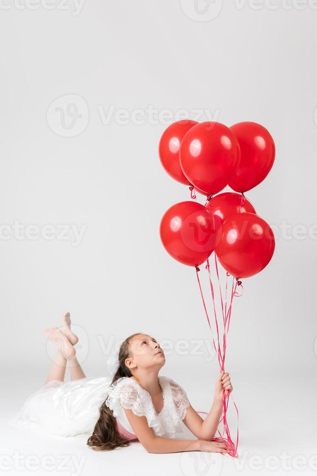 lindo menina em aniversário feriado festa, deitado baixa e segurando vermelho balões dentro mão, olhando acima foto