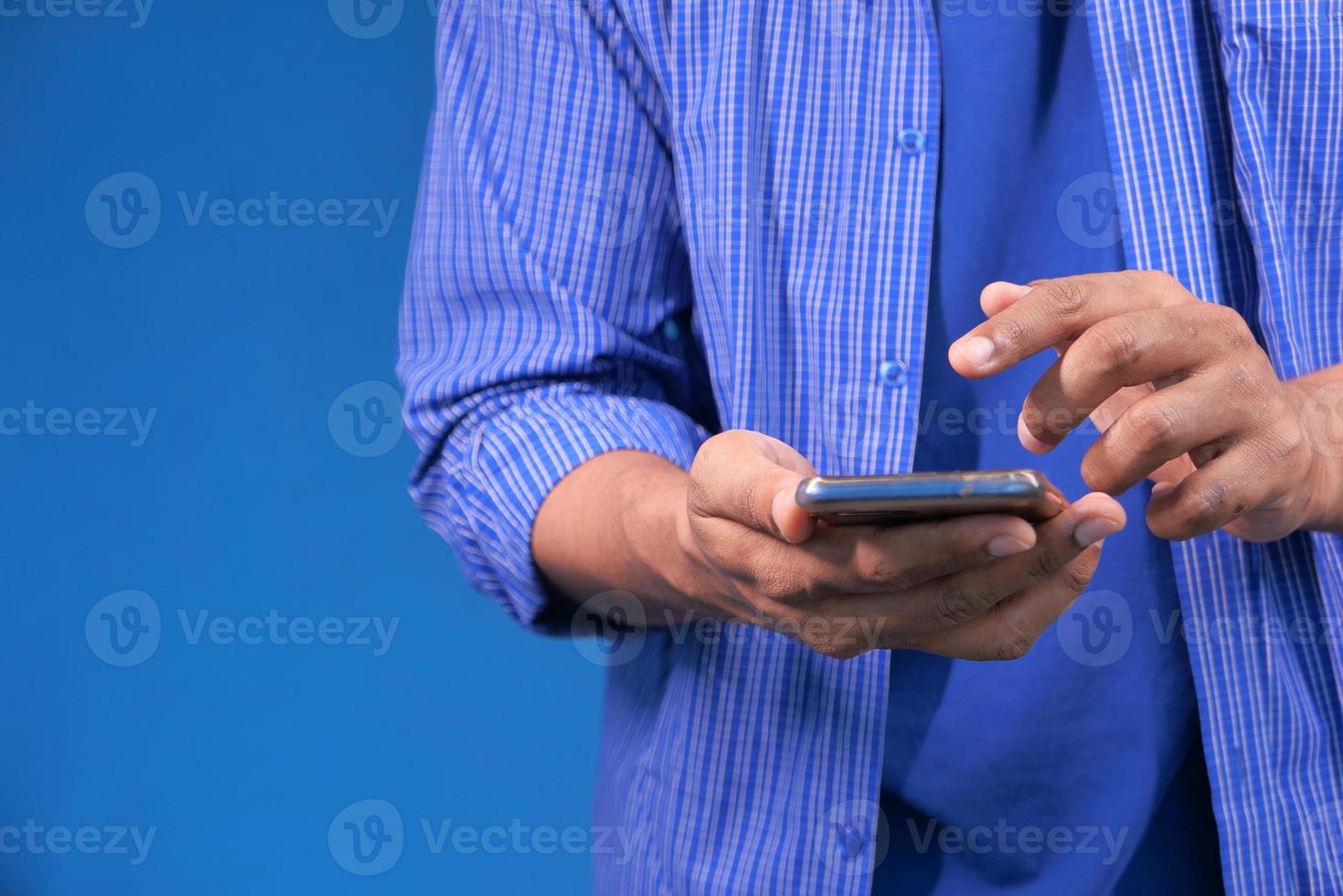 Feche a mão de um jovem usando um telefone inteligente sobre fundo azul foto