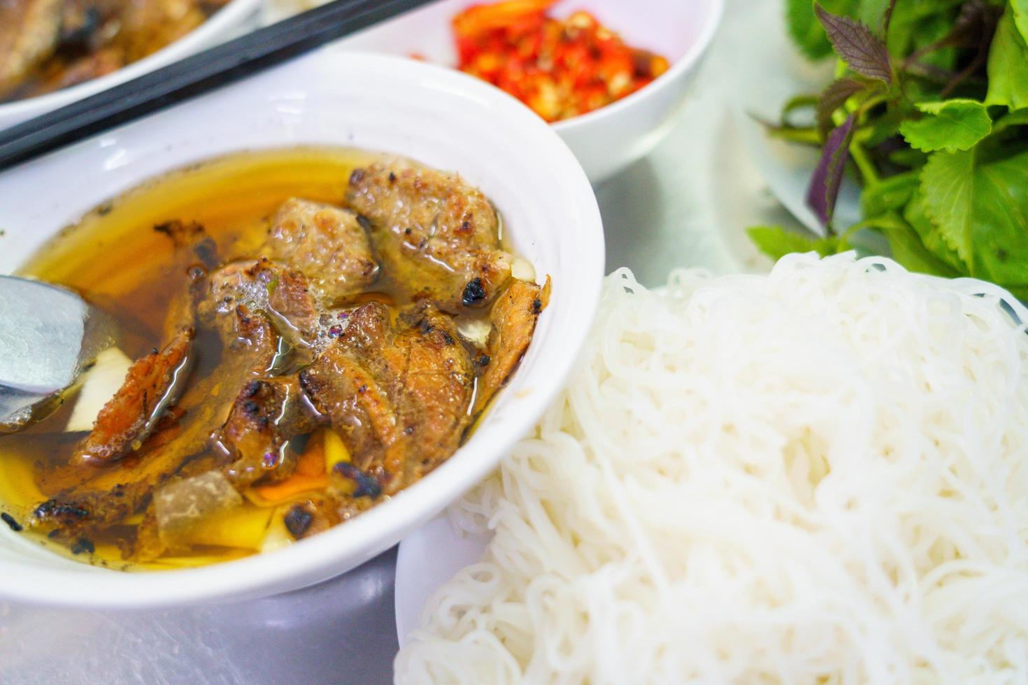 Bun cha com porco grelhado, macarrão de arroz, legumes e sopa na culinária vietnamita foto