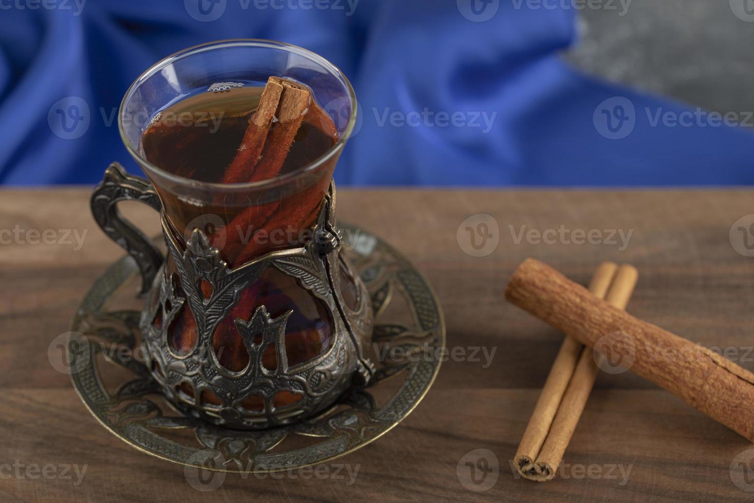 um copo de chá com paus de canela em uma tábua de madeira foto