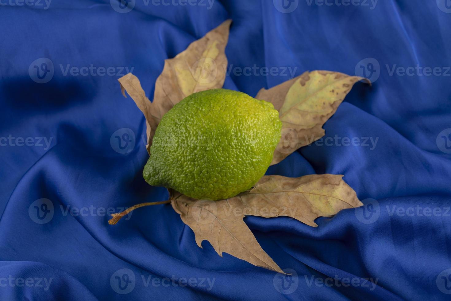 um limão verde maduro em uma folha seca foto