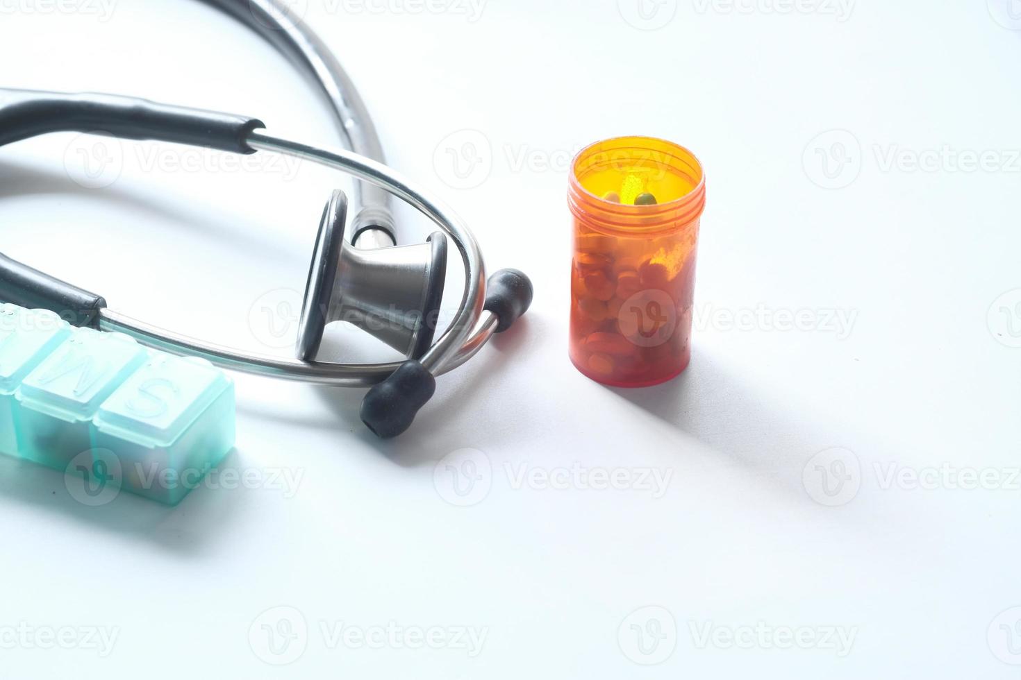 estetoscópio e recipiente de comprimidos no fundo branco foto