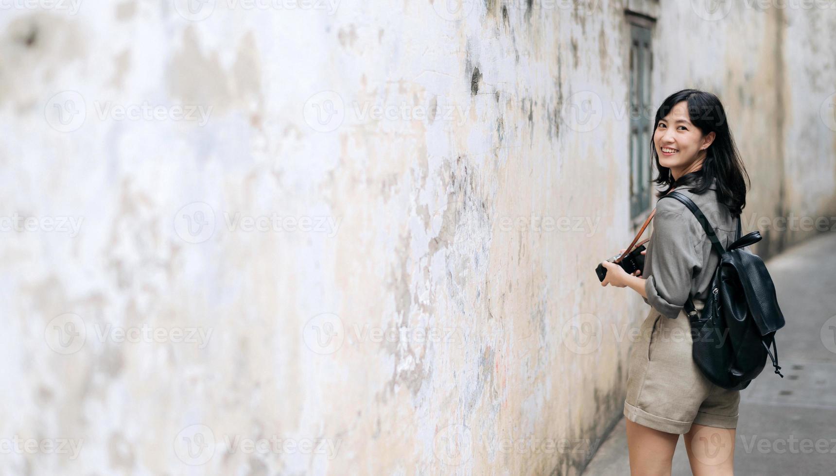 jovem ásia mulher mochila viajante usando digital compactar Câmera, desfrutando rua cultural local Lugar, colocar e sorriso. viajante verificação Fora lado ruas. foto