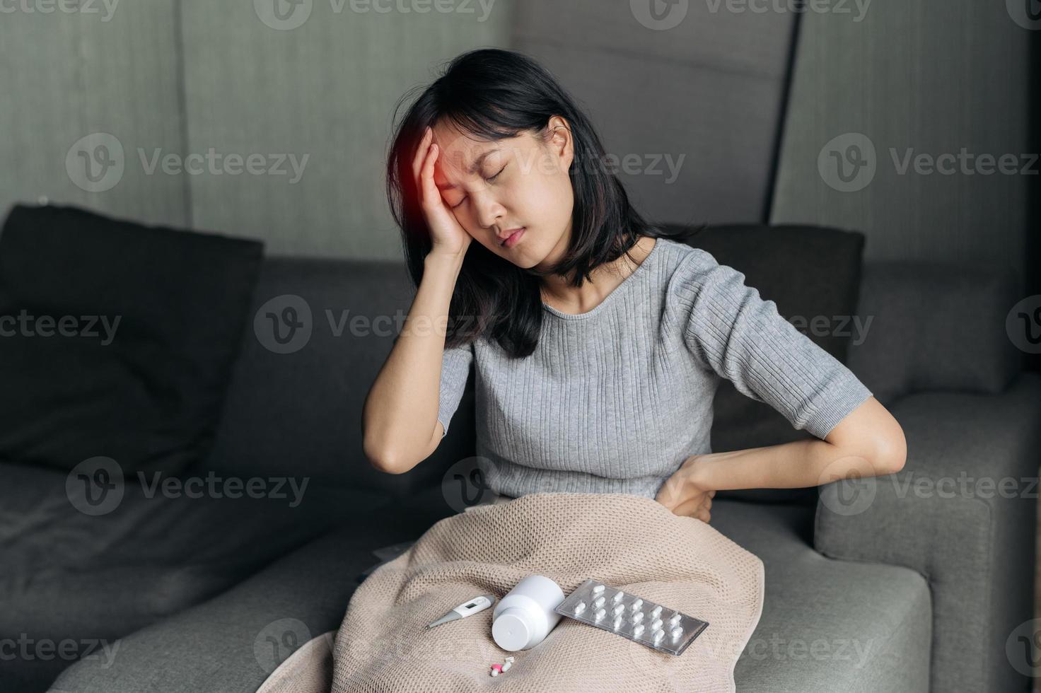 ásia mulher tem uma dor de cabeça em sofá cama. fêmea segurando doloroso cabeça. pessoas com cabeça problema, cuidados de saúde e remédio. foto