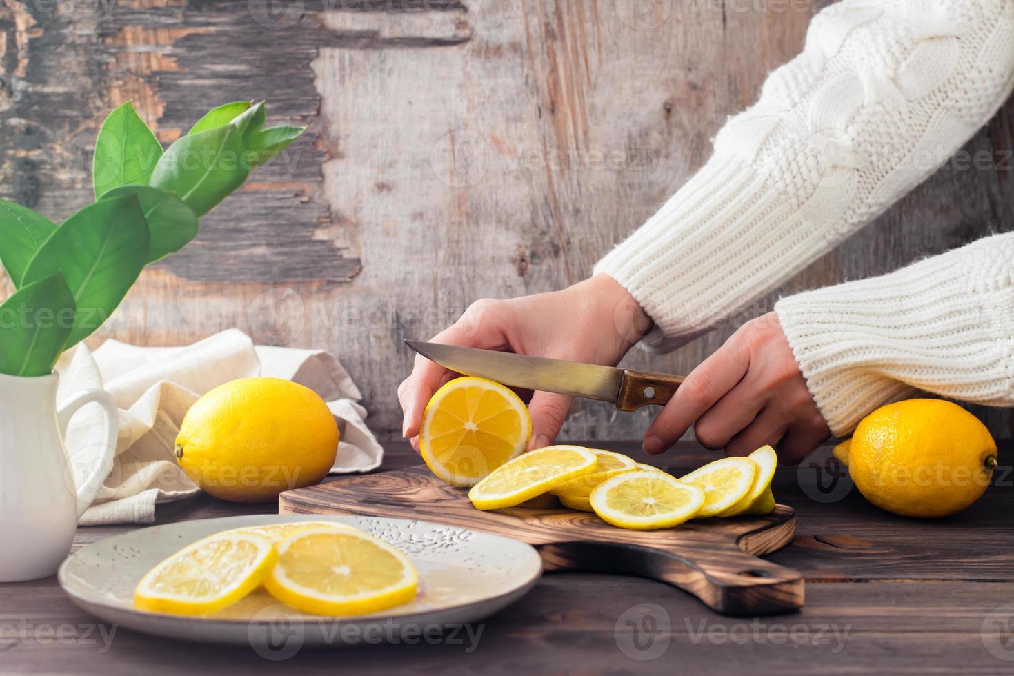 fêmea mãos cortar maduro limões em uma de madeira corte borda e peças em uma prato em a mesa. orgânico nutrição, fonte do vitaminas. foto