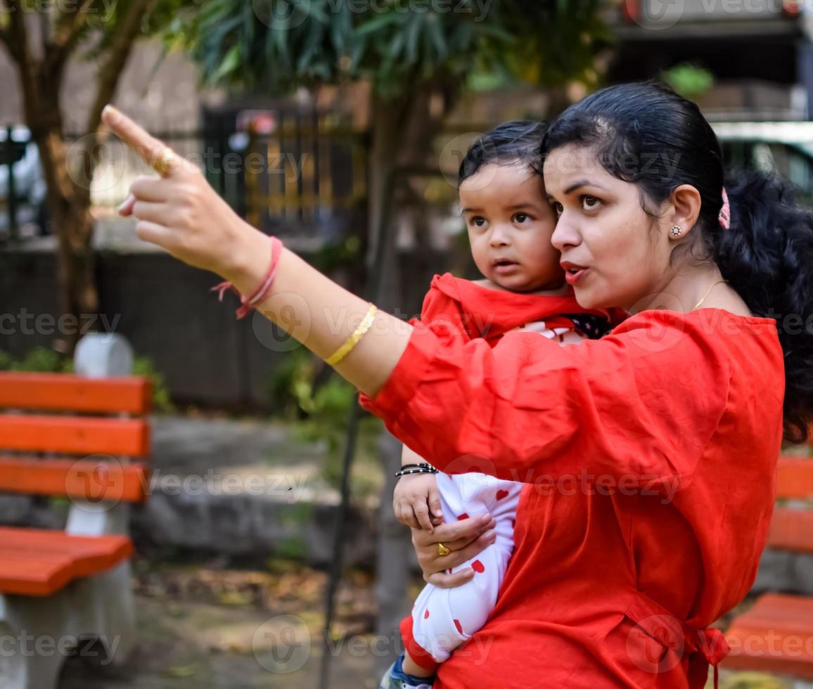 amoroso mãe carregando do dela bebê às sociedade parque. brilhante retrato do feliz mãe segurando criança dentro dela mãos. mãe abraçando dela pequeno 9 meses velho filho. foto