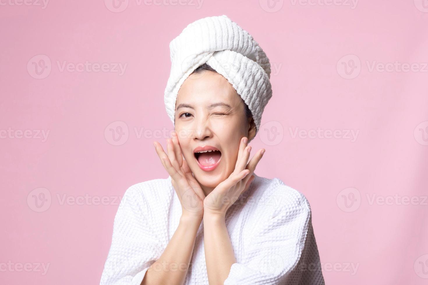 lindo jovem ásia mulher feliz com limpar \ limpo face pele dentro toalha e roupão de banho, spa terno em Rosa fundo. cuidados com a pele, tratamento, bem estar terapia, facial Cuidado, beleza fêmea saúde, cosmetologia conceito foto