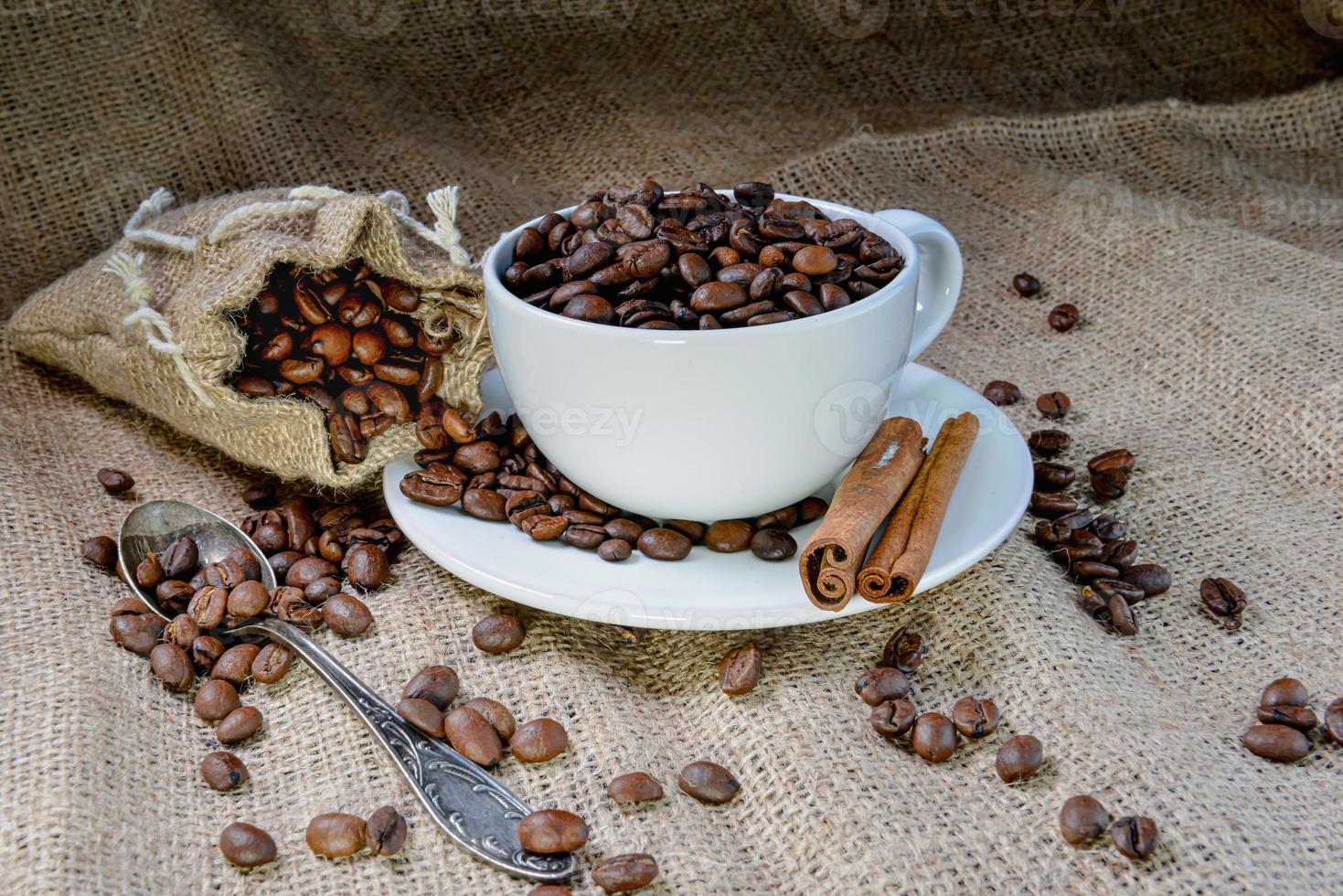 caneca de café branca cheia de grãos de café orgânico e paus de canela em tecido de linho foto