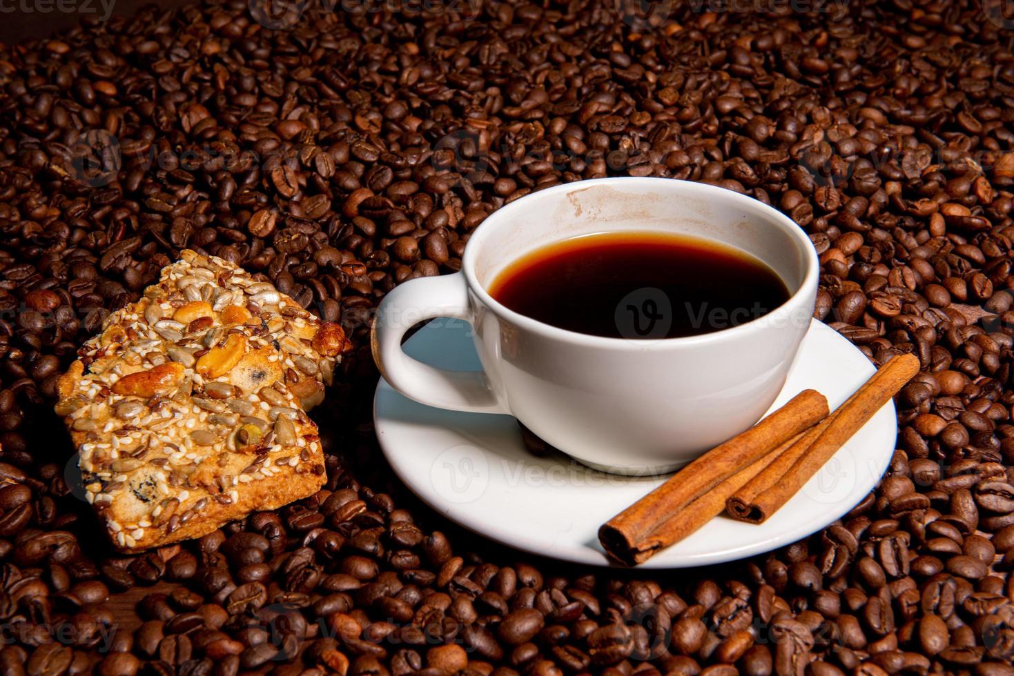 caneca de café branco, paus de canela e biscoitos no fundo de grãos de café foto