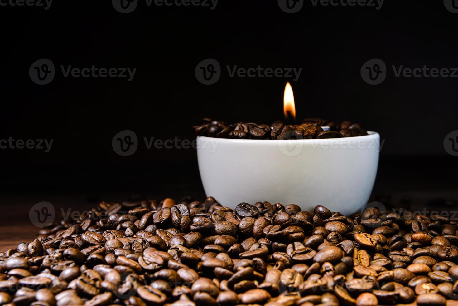 xícara de café branco cheia de grãos de café e vela acesa no topo da pilha de grãos de café foto