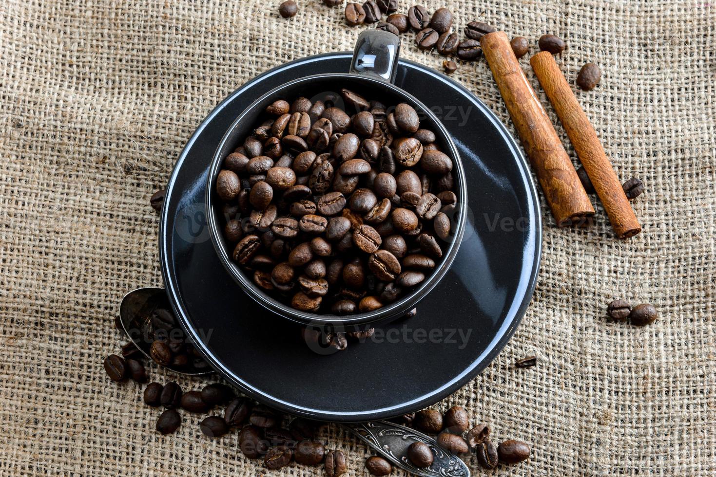 caneca de café preta cheia de grãos de café orgânico e paus de canela em tecido de linho foto