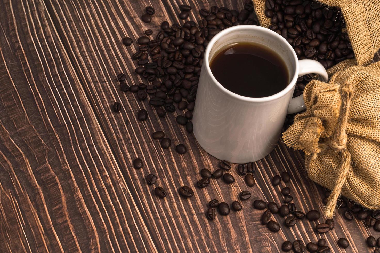 uma caneca de café e grãos de café em uma mesa de madeira foto