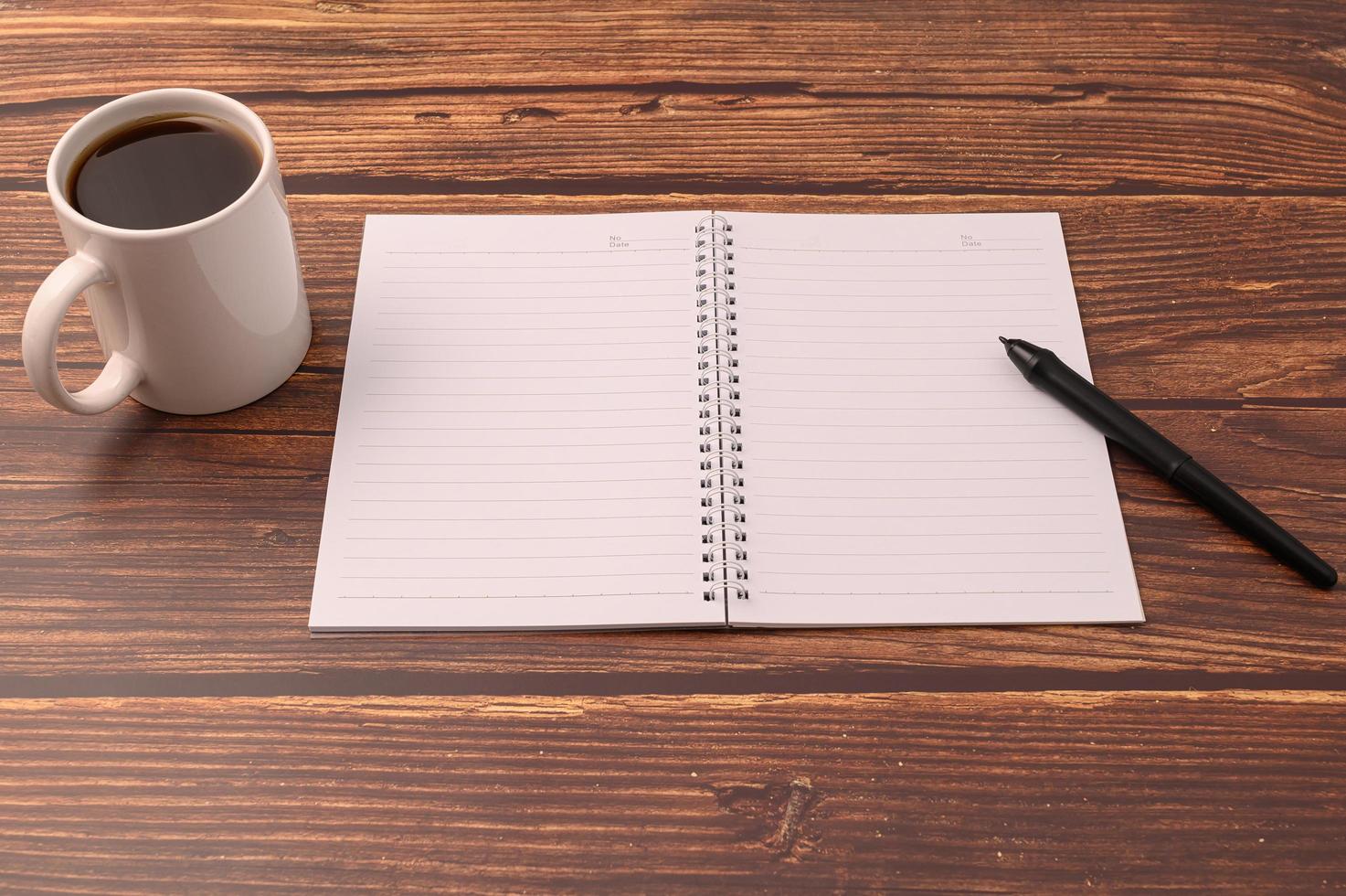 café e um caderno com uma caneta sobre uma mesa de madeira foto