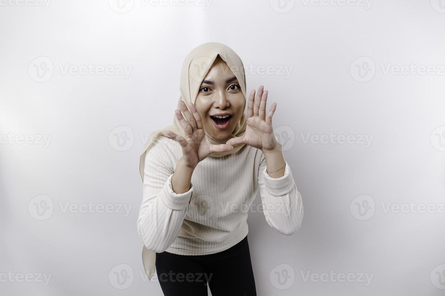 jovem lindo ásia muçulmano mulher vestindo uma lenço de cabeça gritando e gritando alto com uma mão em dela boca. comunicação conceito. foto
