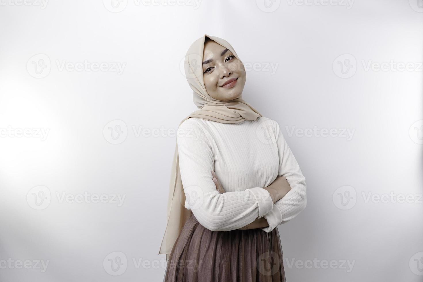 uma confiante sorridente ásia muçulmano mulher vestindo hijab em pé com braços guardada e olhando às a Câmera isolado sobre branco fundo foto