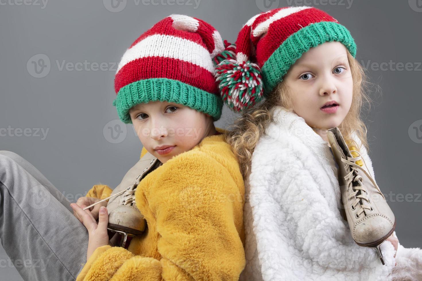 lindo pequeno menina e Garoto dentro tricotado Natal chapéus estão sentado com seus costas para cada de outros e sorridente em uma cinzento fundo. feliz Natal crianças. foto