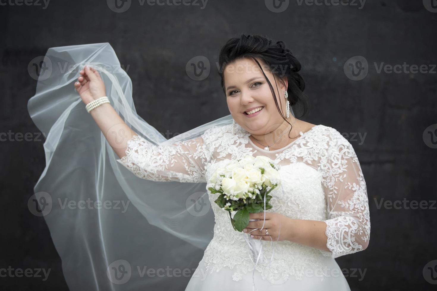 retrato do uma cheio noiva com uma acenando véu com uma ramalhete em uma Sombrio fundo. foto